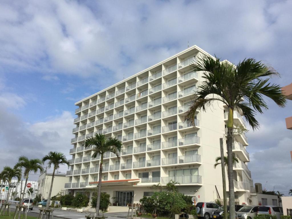 丰见城市大花园冲绳酒店的一座白色的大建筑,前面有棕榈树