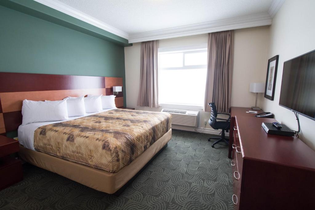 ManningNova Inn Manning的酒店客房配有一张床、一张书桌和一台电视。