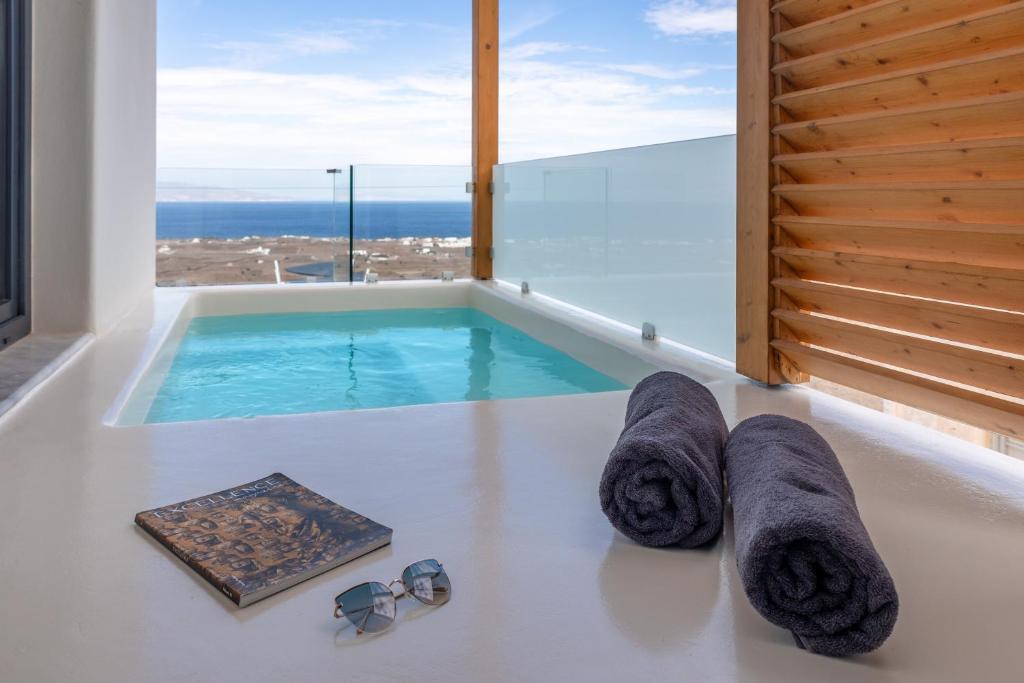 伊亚North Wind Luxury Suites的带小型游泳池的房间，配有太阳镜和毛巾