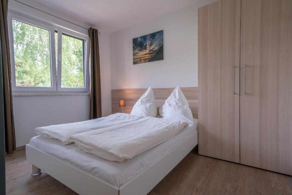 柏林Ferienpark Rübezahl am Müggelsee, Haus 20 Mohn mit eigener Sauna, idealer Ort für Natur- und Erholungssuchende, für Radfahrer und Familien mit Kindern的卧室里有一张铺着白色床单的床和一扇窗户