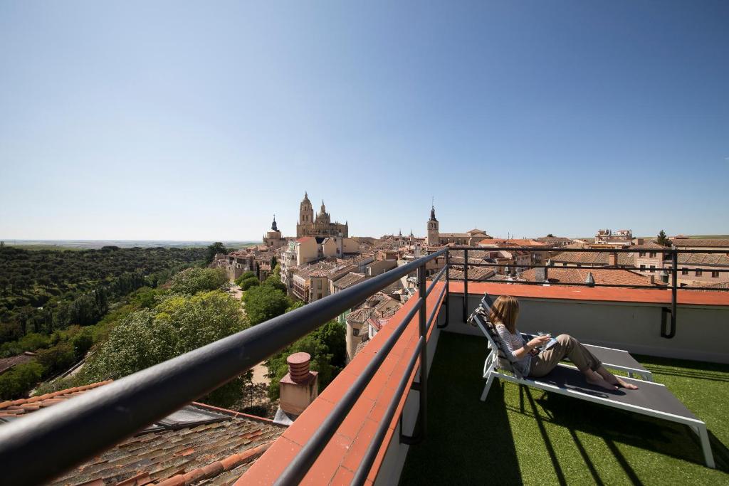 塞哥维亚Real Segovia by Recordis Hotels的坐在阳台上的女人坐在椅子上,看着城市