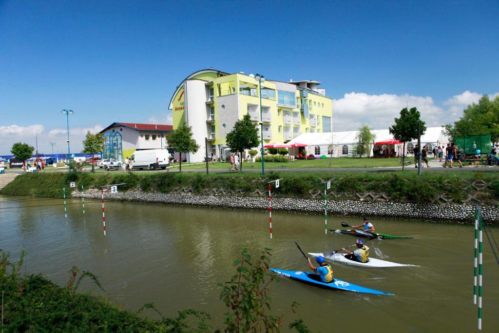 布拉迪斯拉发迪沃卡沃达酒店及公园的三人在河上划皮艇,有一栋建筑