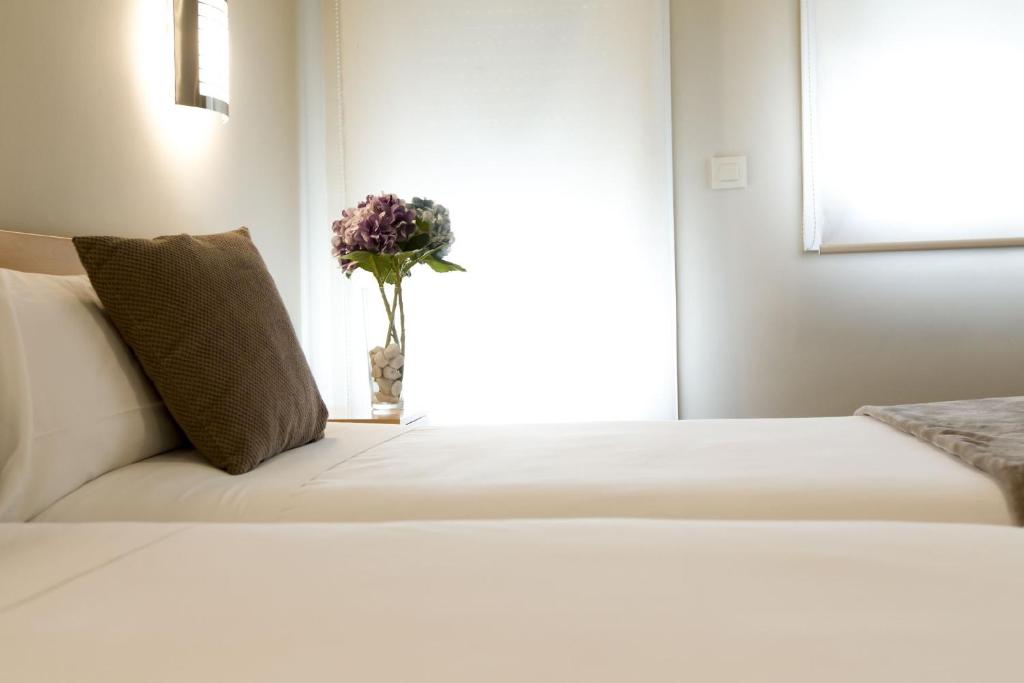 梅里达Vettonia Hotel的白色的床,花瓶上放着一朵花
