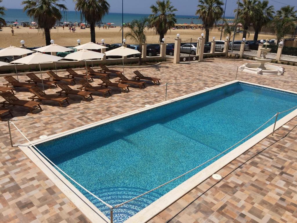 恩佩多克莱港Hotel Riviera Palace的海滩旁的游泳池配有椅子和遮阳伞
