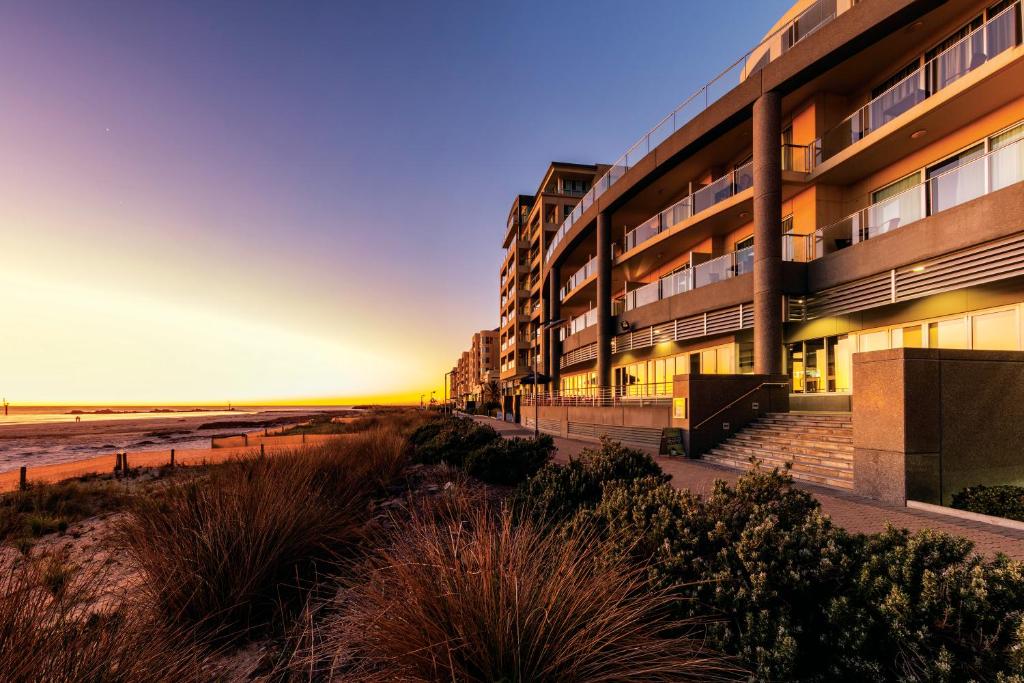 阿德莱德Oaks Glenelg Plaza Pier Suites的日落时在海滩上的公寓大楼