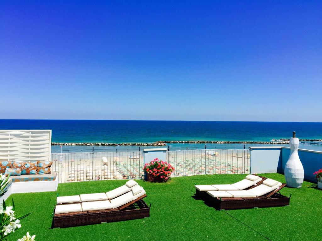 里米尼Residence Frontemare的两张白色沙发,坐在靠近大海的草地上