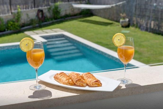 希贝尼克Luxury Apartment with Heating Pool的两杯橙汁和羊角面包放在泳池附近的桌子上