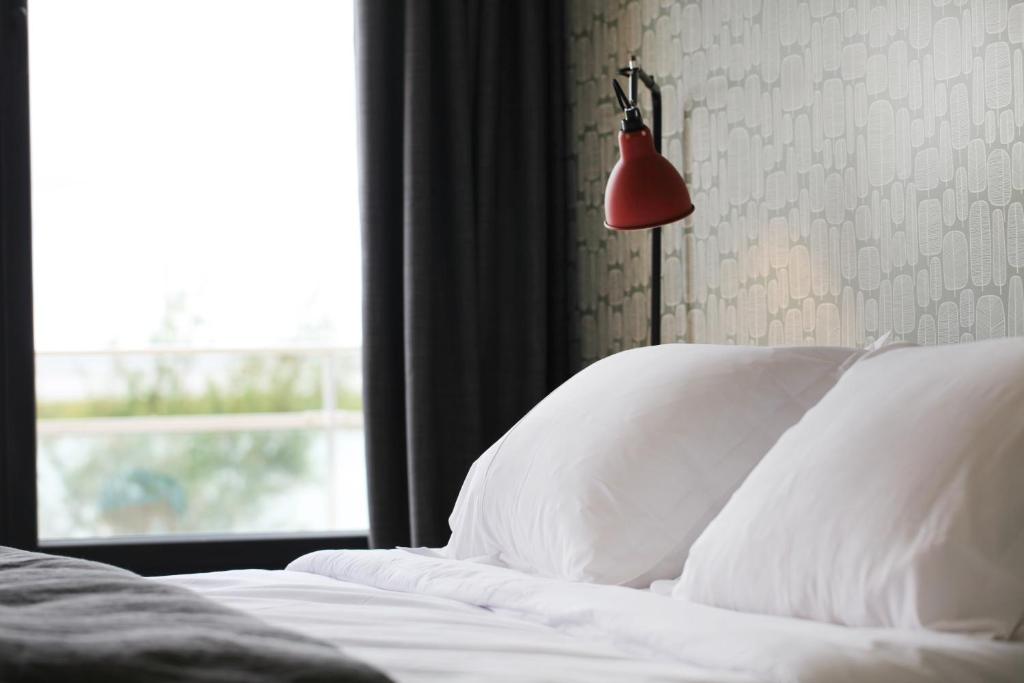 马雷讷Dormir sur la Plage的一间卧室配有带白色枕头和红色灯的床。