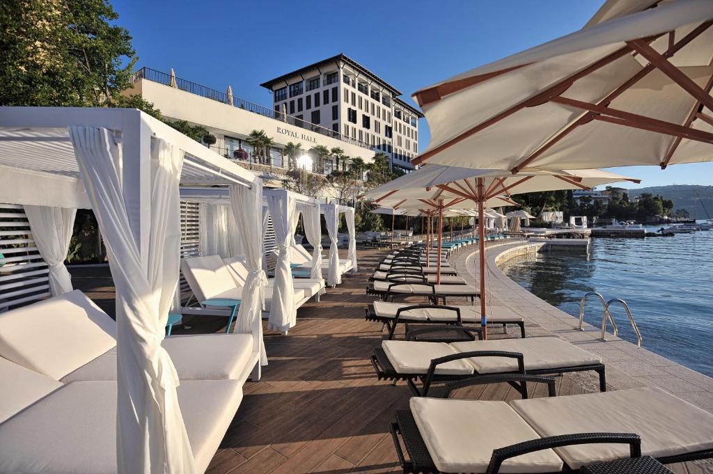 奥帕提亚Amadria Park Hotel Royal的水边的一排白色椅子和遮阳伞