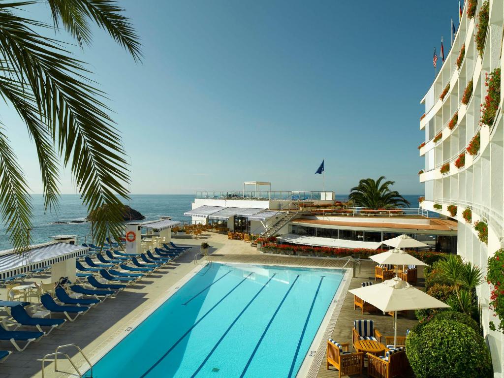 滨海托萨Gran Hotel Reymar的一个带椅子的游泳池,背景是大海