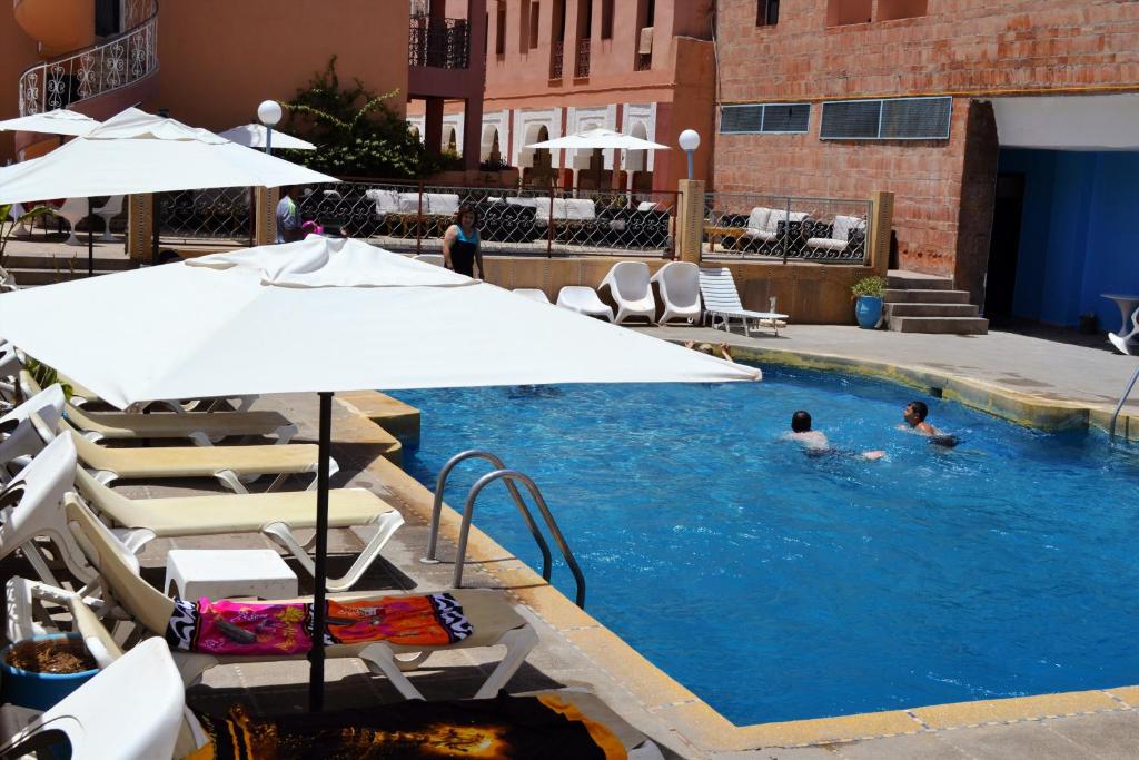 马拉喀什Le Grand Hotel Tazi的两人在带遮阳伞的游泳池游泳