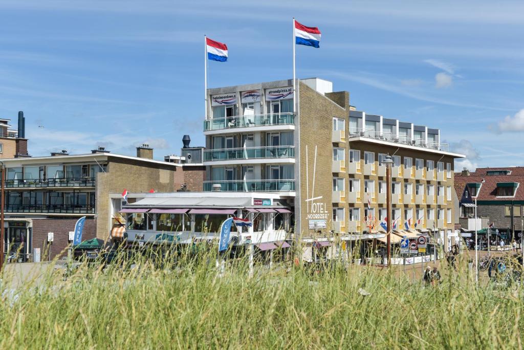 滨海卡特韦克北海酒店的停在有两面旗帜的建筑前面的公共汽车
