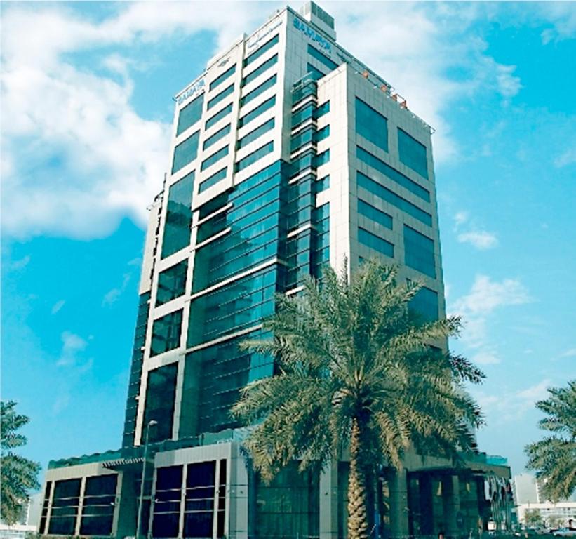 迪拜迪尔拉萨玛雅酒店的一座高大的建筑,前面有一棵棕榈树