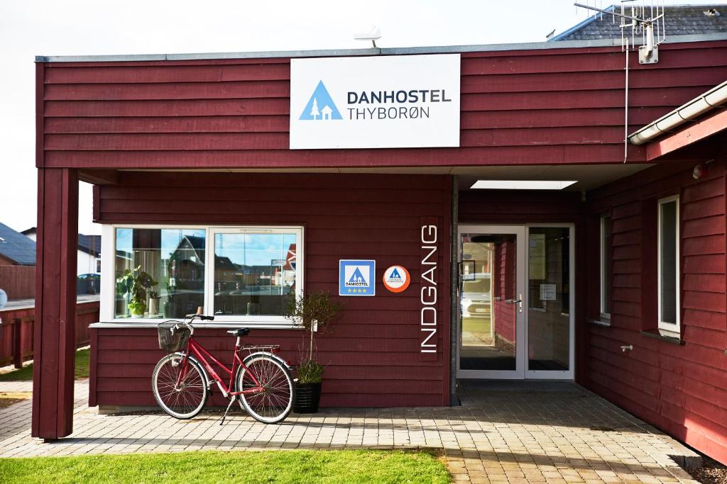 曲博伦Danhostel Thyborøn的一座红色的建筑,外面停有一辆自行车