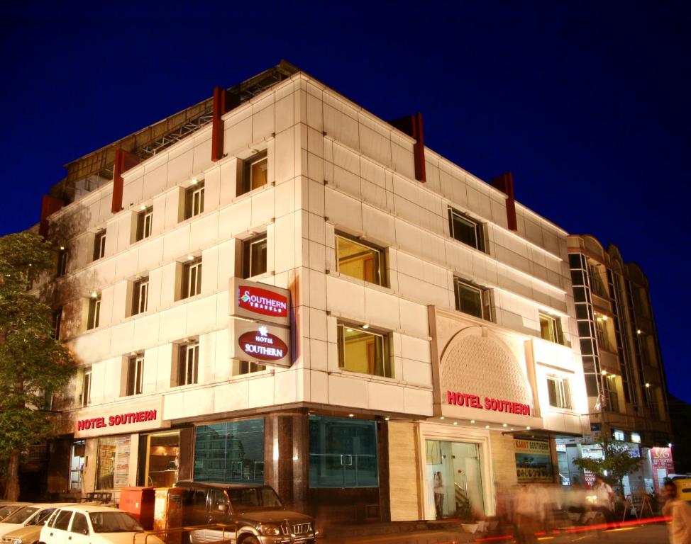 新德里南方酒店的一座白色的大建筑,前面有汽车停放