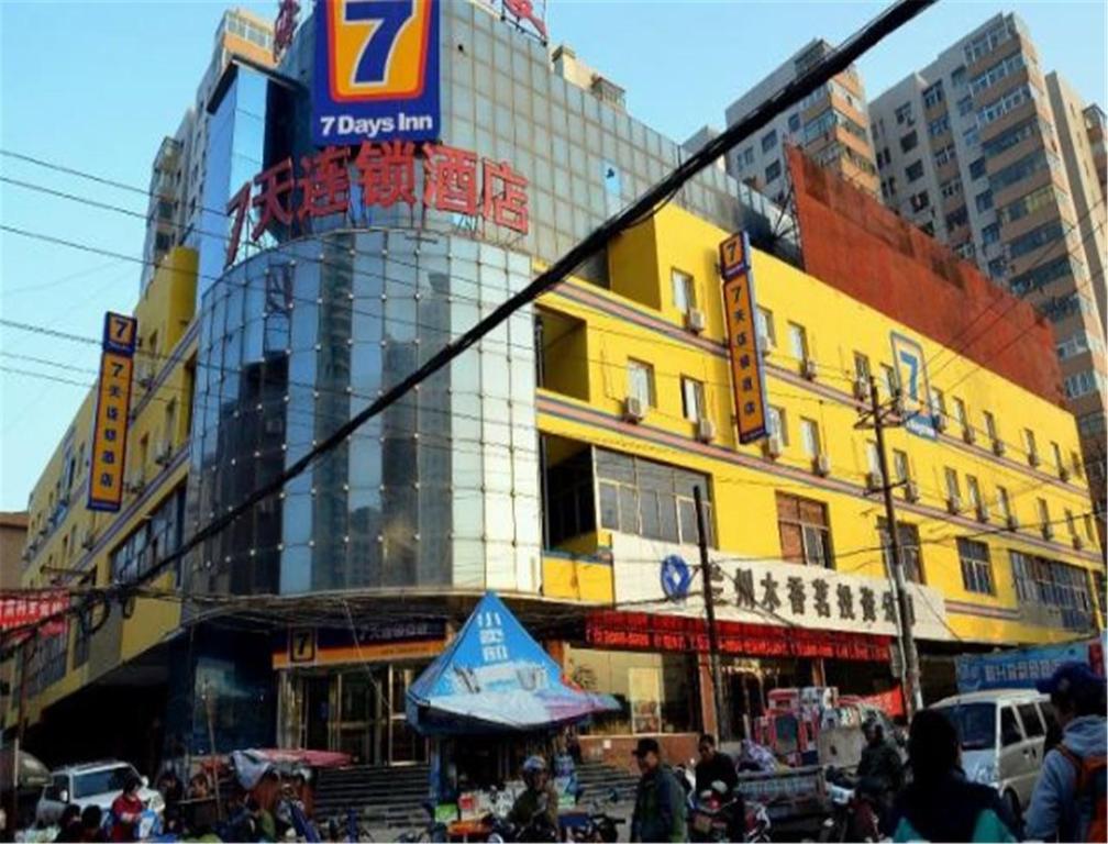 兰州七天连锁酒店兰州西站店的一座黄色的建筑,前面的人在步行