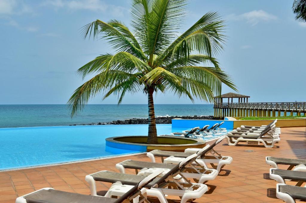 圣多美佩斯塔纳圣多美酒店的游泳池旁的一排躺椅和一棵棕榈树