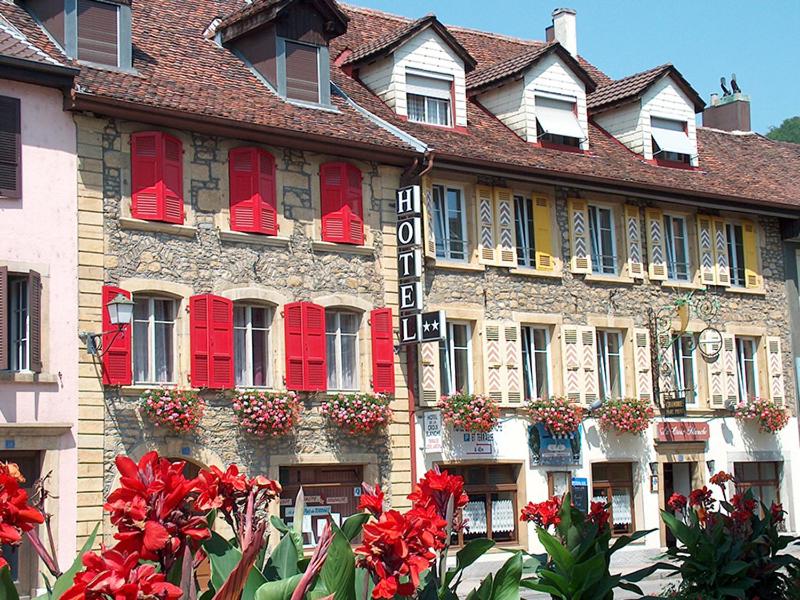 Cressier克鲁瓦-布兰奇酒店的一座建筑前方有红色窗户和鲜花