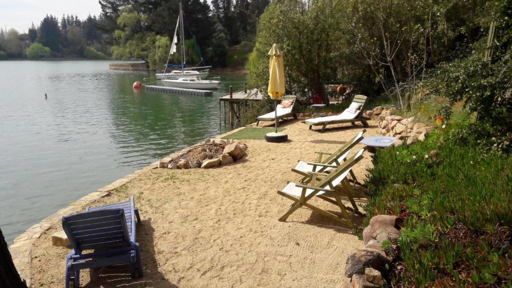 拉佩尔湖Cabaña de Adobe en Lago Rapel的湖岸上的一组椅子和一把伞