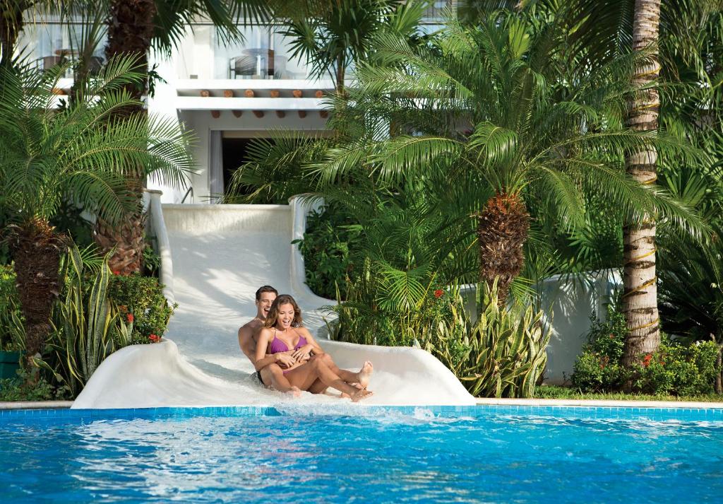 科苏梅尔Secrets Aura Cozumel - Adults Only的坐在游泳池旁白色滑梯上的男女