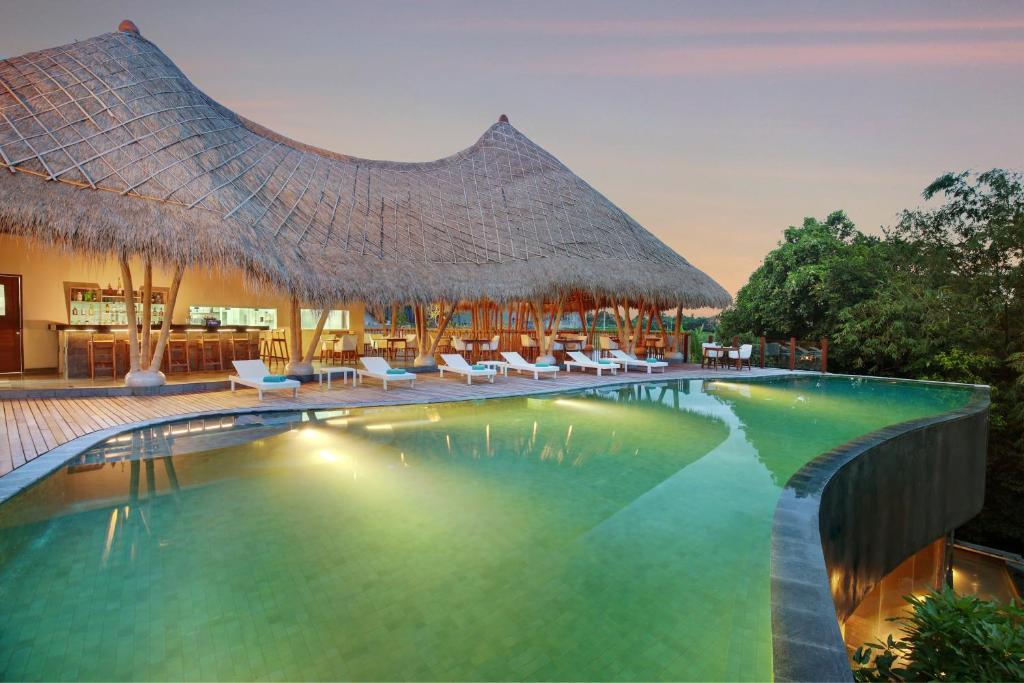 坎古Theanna Villa and Spa Canggu的一个带椅子和茅草屋顶的度假游泳池
