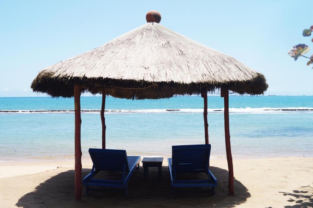 洛美罗宾逊海滨酒店的海滩上一把稻草伞下的两把椅子和一张桌子