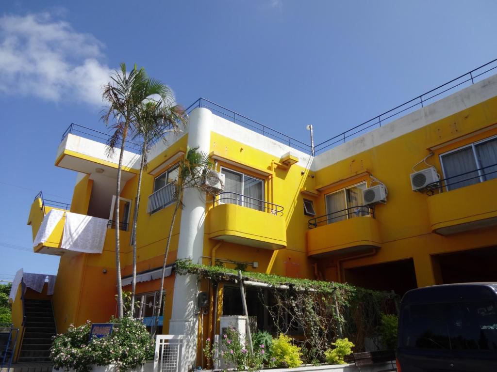 宫古岛Pension Orange Box的一座黄色的建筑,前面有棕榈树
