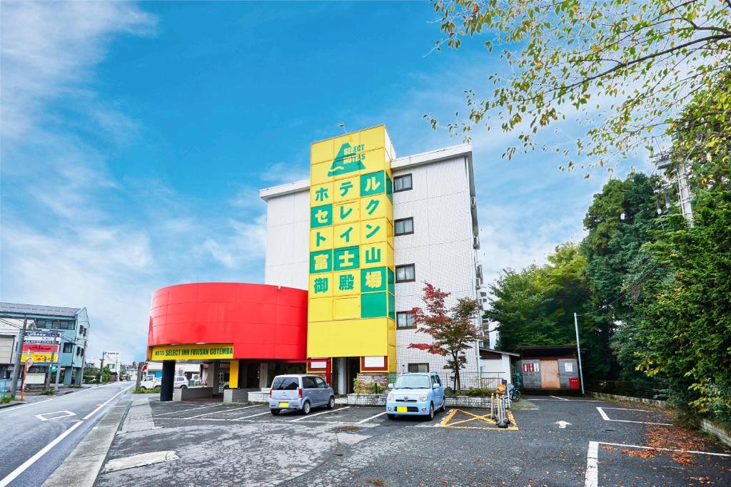 御殿场市富士山御殿场市精选旅馆的一座黄色和白色的建筑,停车场内有车辆停放