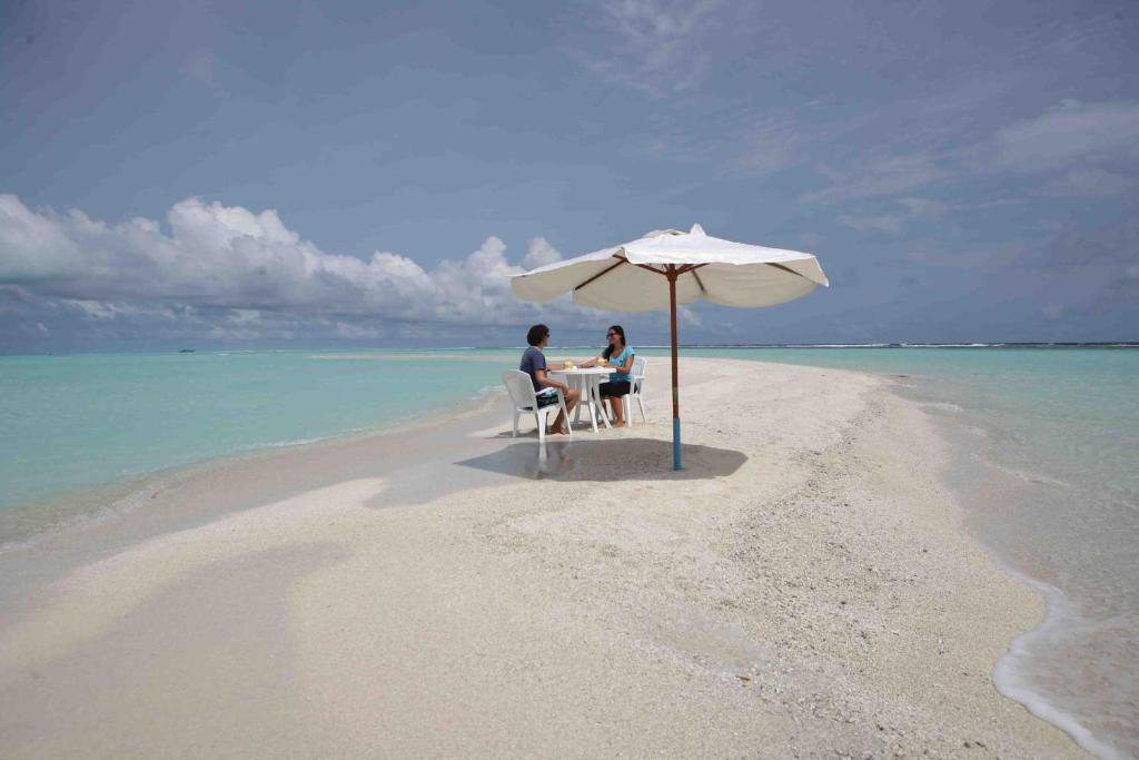 福拉杜岛阿佐什旅游宾馆的两人坐在海滩上一把伞下的桌子上