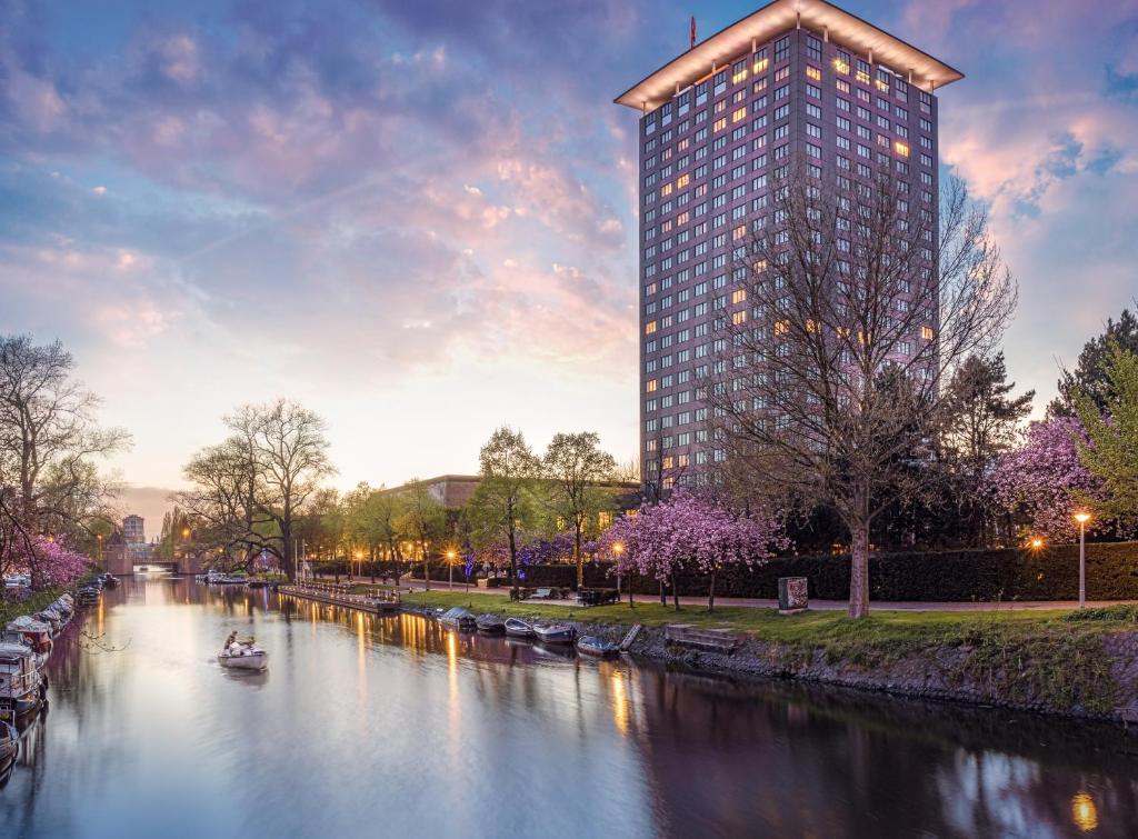 阿姆斯特丹阿姆斯特丹大仓酒店 - 世界一流酒店的一条高大的建筑物,旁边是一条有船的河流
