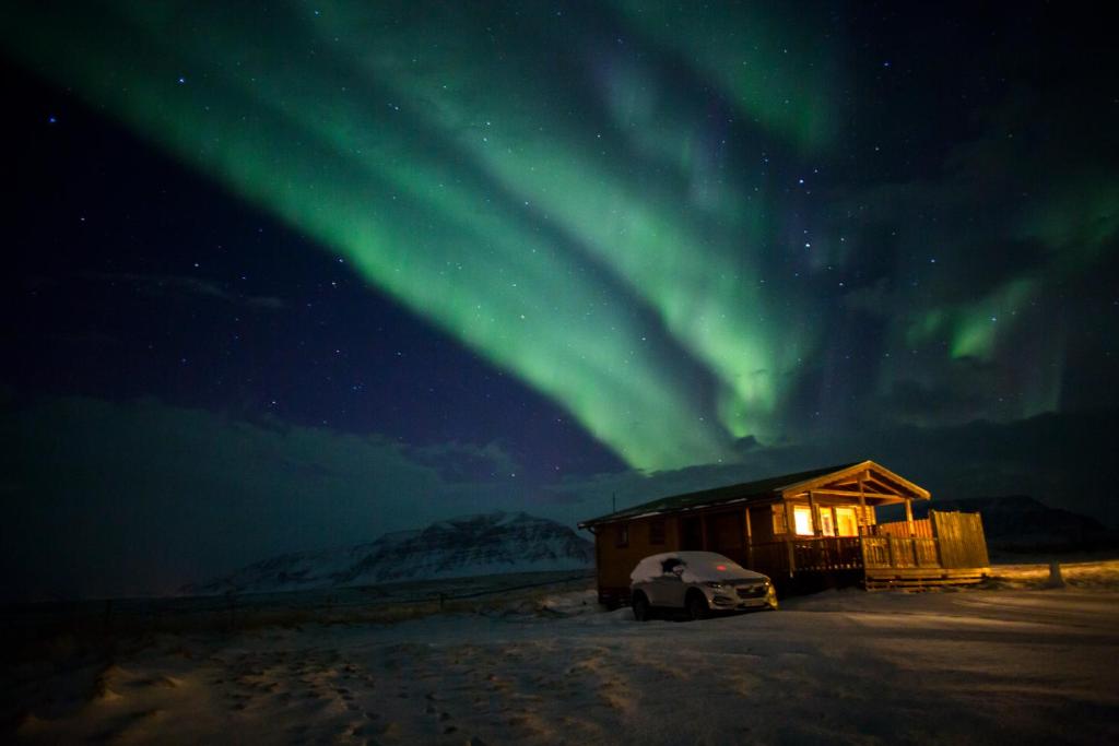 博尔加内斯斯诺拉斯塔迪尔农家乐的小屋,有车停在北极光下