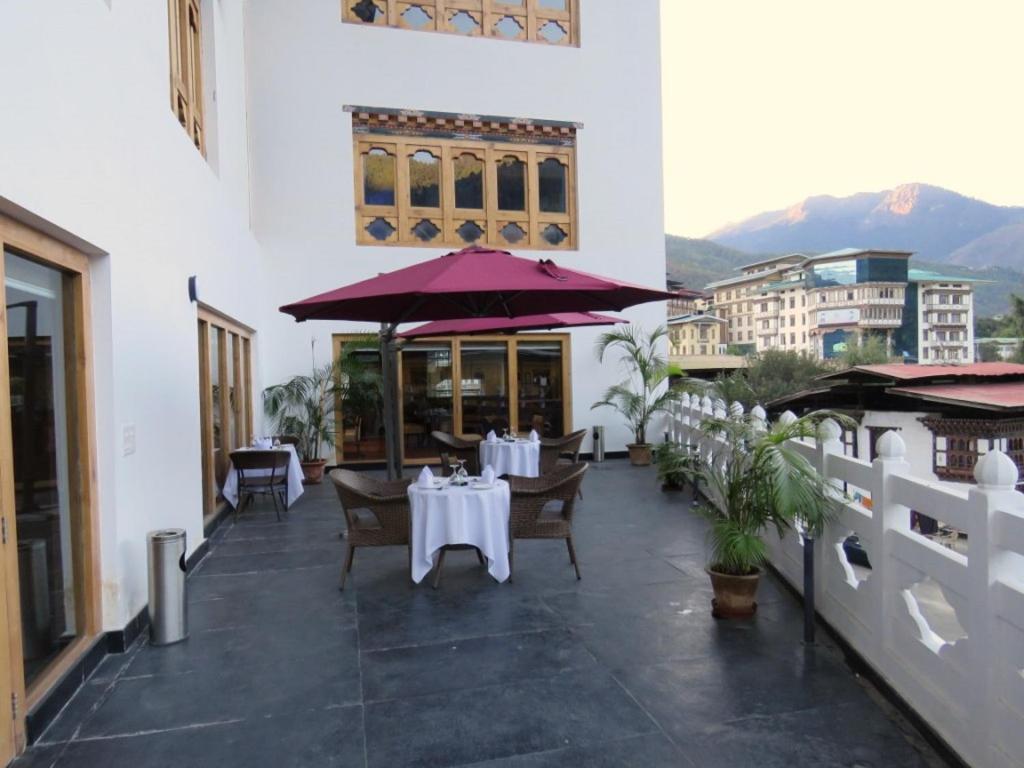 廷布廷布城市酒店的餐厅配有白色的桌椅和紫色的遮阳伞