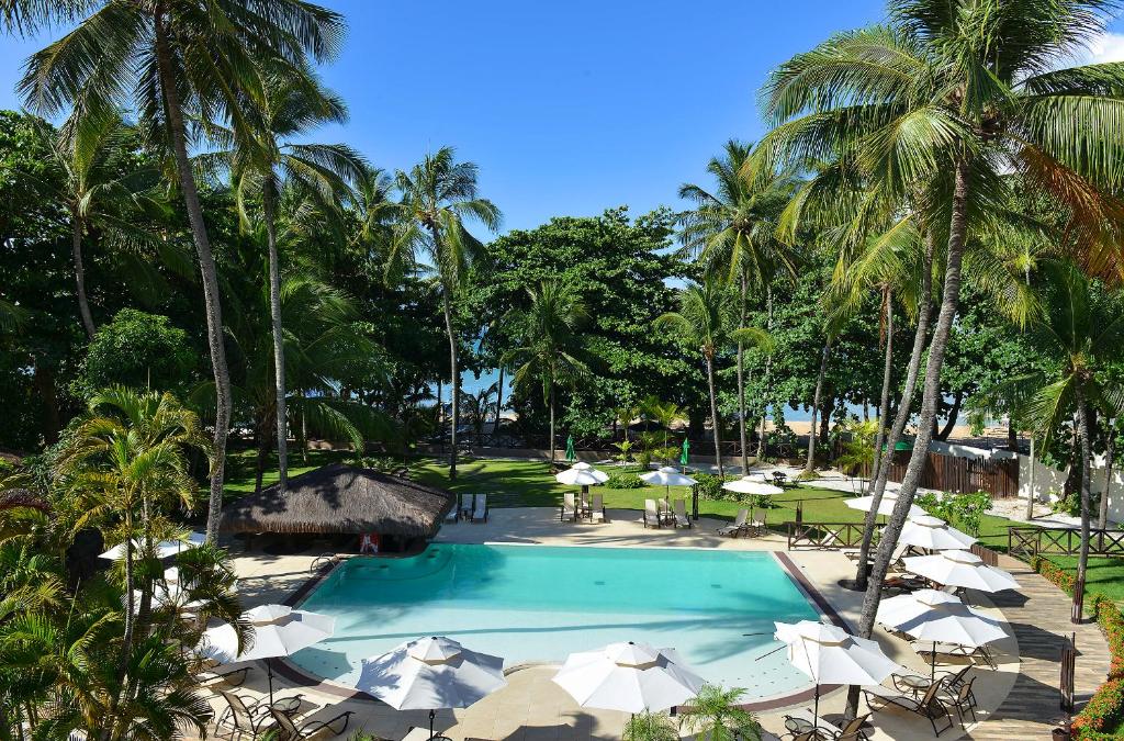 萨尔瓦多Iara Beach Hotel Boutique的一个带遮阳伞和桌子的游泳池以及棕榈树