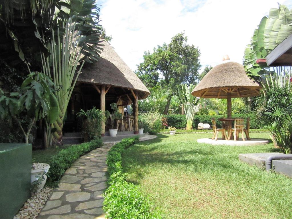恩德培Precious Guesthouse的花园设有茅草小屋、桌子和遮阳伞