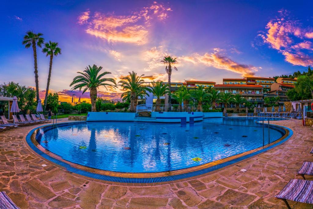 拉戈曼德拉Lagomandra Hotel and Spa的棕榈树和日落度假村的游泳池