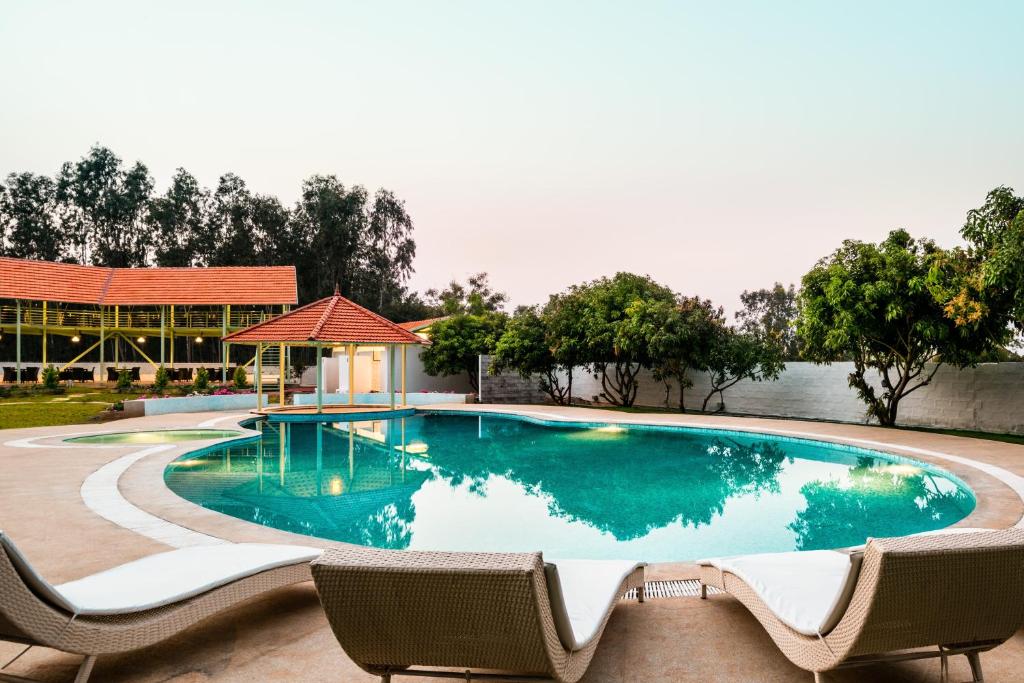德瓦纳哈利-班加罗尔费斯塔活动场所度假村的一座带两把椅子的游泳池以及一座建筑