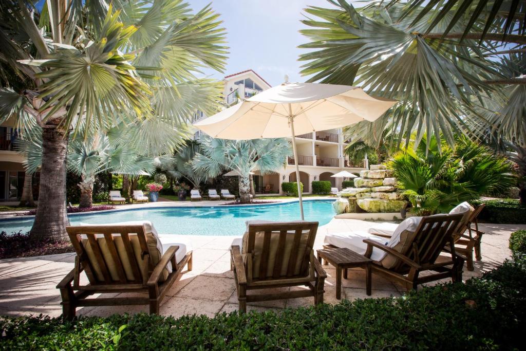 格雷斯湾德尔马尔别墅酒店的游泳池旁的两把椅子和一把遮阳伞
