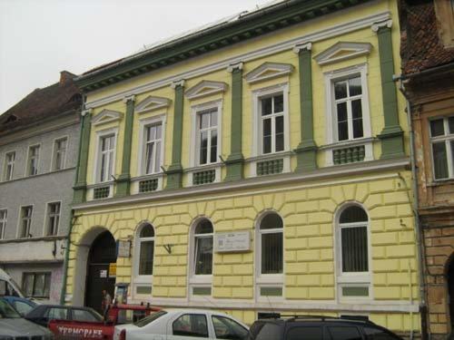 布拉索夫特里萨之家酒店的一座黄色和绿色的建筑,前面有汽车停放