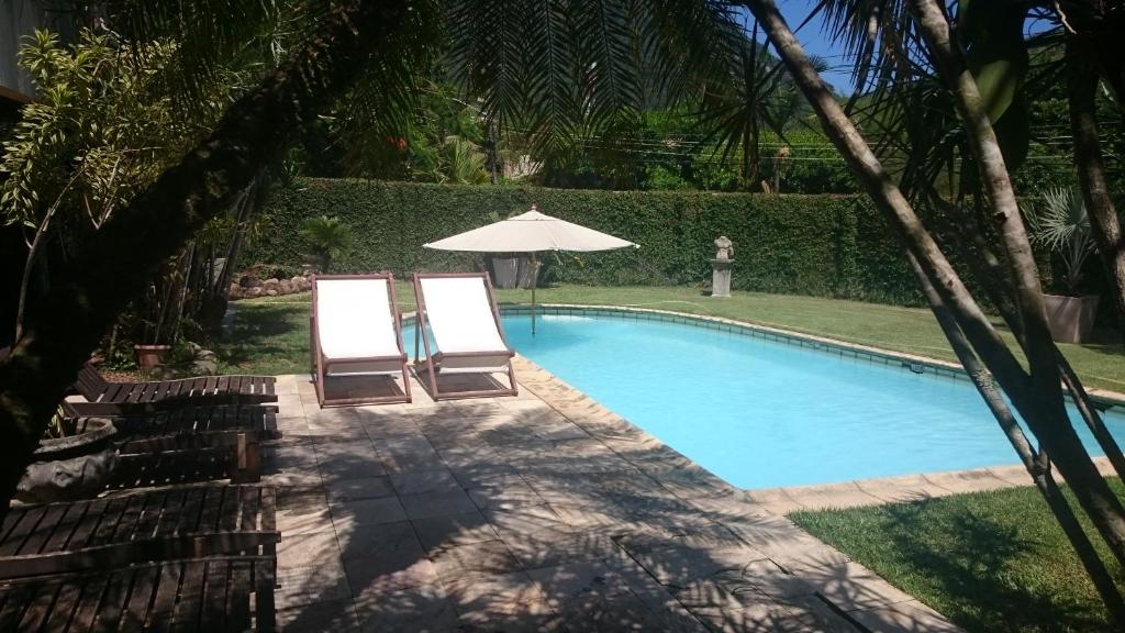 里约热内卢瑞卡萨坦哈哥住宿加早餐旅馆的游泳池旁的两把椅子和一把遮阳伞