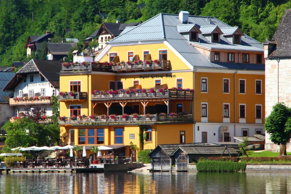 哈尔施塔特格鲁纳鲍姆酒店的一座黄色的建筑,在水边的阳台摆放着椅子