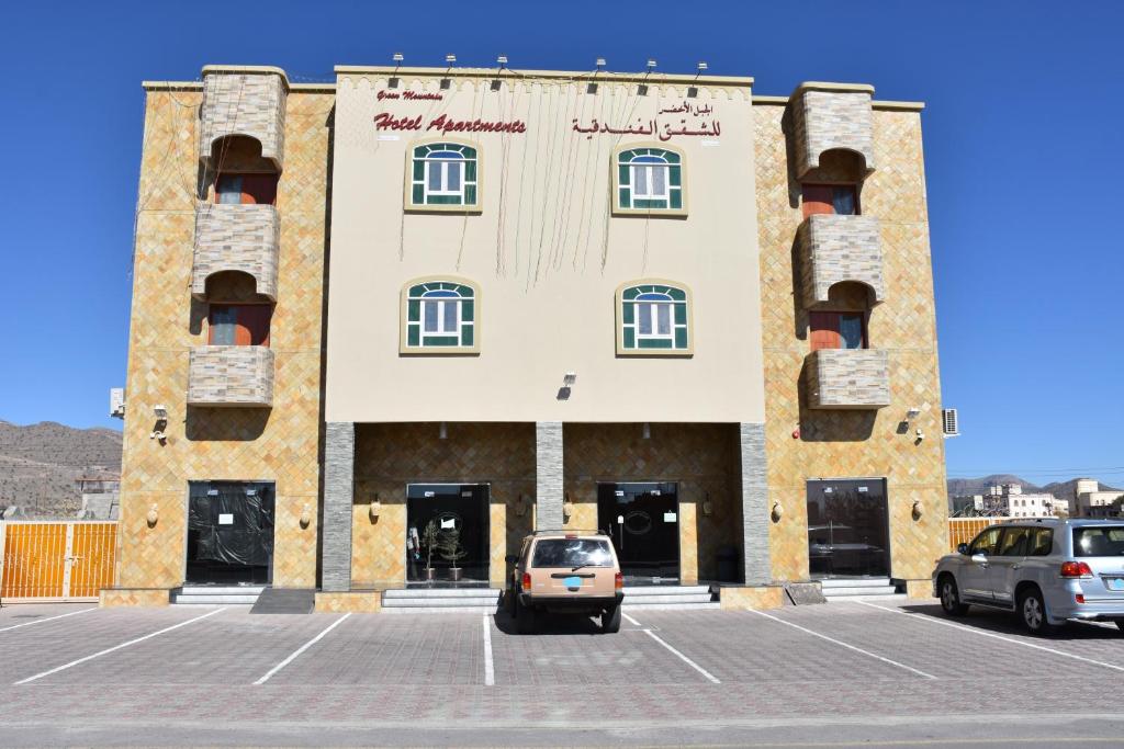 Al ‘AqarGreen Mountain Hotel Apartments的停车场内有车辆的建筑物