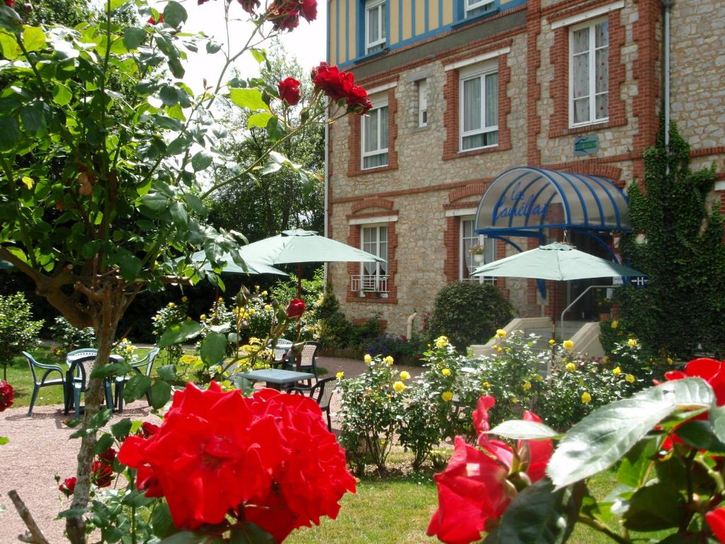 巴尼奥勒德日洛恩布里特茶花酒店的一座花园,在一座建筑前方,花园内摆放着红色玫瑰和遮阳伞