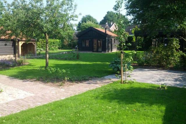 迪弗尔Vakantiehuisje met bedstee的一座带房子和绿草的院子