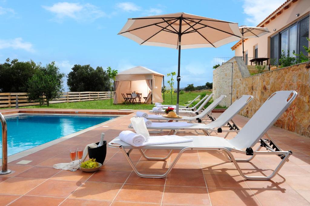 马鲁拉斯Kivotos Villa的游泳池旁的天井配有椅子和遮阳伞。