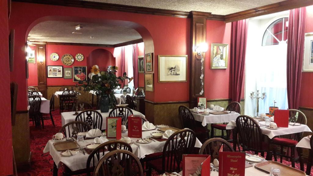 圣赫利尔泽西莫宁顿酒店的一间设有桌椅的餐厅,位于带红色墙壁的房间