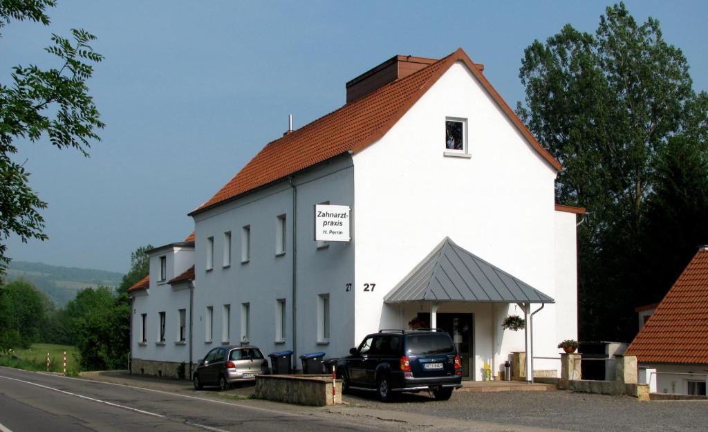 Bliesmengen-Bolchen佩兰酒店的一座白色的建筑,前面有汽车停放