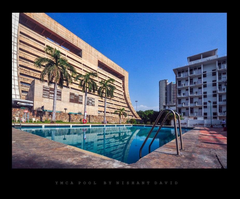 新德里新德里YMCA观光客旅馆的棕榈树建筑前的游泳池