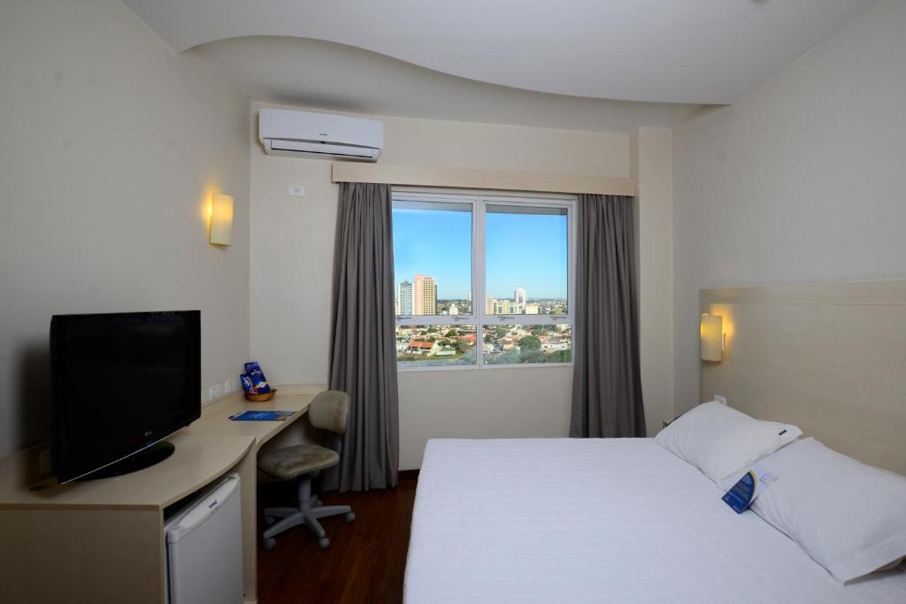 隆德里纳Golden Blue Hotel的配有一张床、一张书桌和一扇窗户的酒店客房