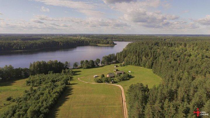 MindūnaiKaimo Turizmo Sodyba Šniūrai的湖畔田野上房屋的空中景观