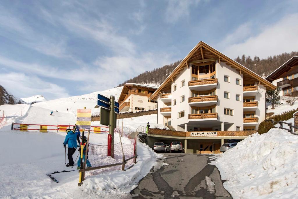 萨姆瑙恩Appartements Garni Alpin Live的两个人站在滑雪小屋前的雪地里